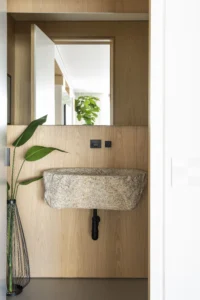 The washroom at Apartamento AM seen through the doorway, with its stone basin set against oak panelling and a mirror above