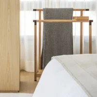 Wooden valet stand holding a grey knit throw beside the bed in the suite at Apartamento AM