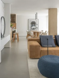 Integrated social area at Apartamento AM, with a tan suede sofa, blue cushions and pouf, and the dining table and kitchen counter beyond