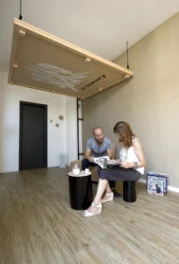 The raised bed panel tilted above two residents reading in the living area of Space is Luxury