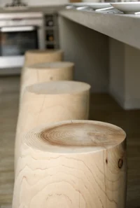 Close-up of the cypress log stools and the concrete counter edge, with the kitchen beyond, at Space is Luxury