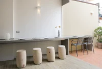 The concrete counter set for a meal, with cylindrical log stools inside and metal chairs on the terrace beyond, at Space is Luxury
