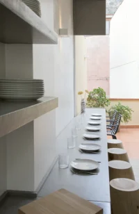 Long concrete table set with plates and glasses running toward the terrace, beside cantilevered concrete shelves at Space is Luxury