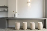 Cypress log stools lined up under the concrete counter, lit by a single wall light, at Space is Luxury