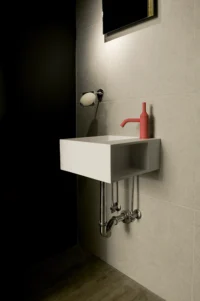 Compact bathroom at Space is Luxury with a wall-hung white basin, exposed chrome pipework and a red tap