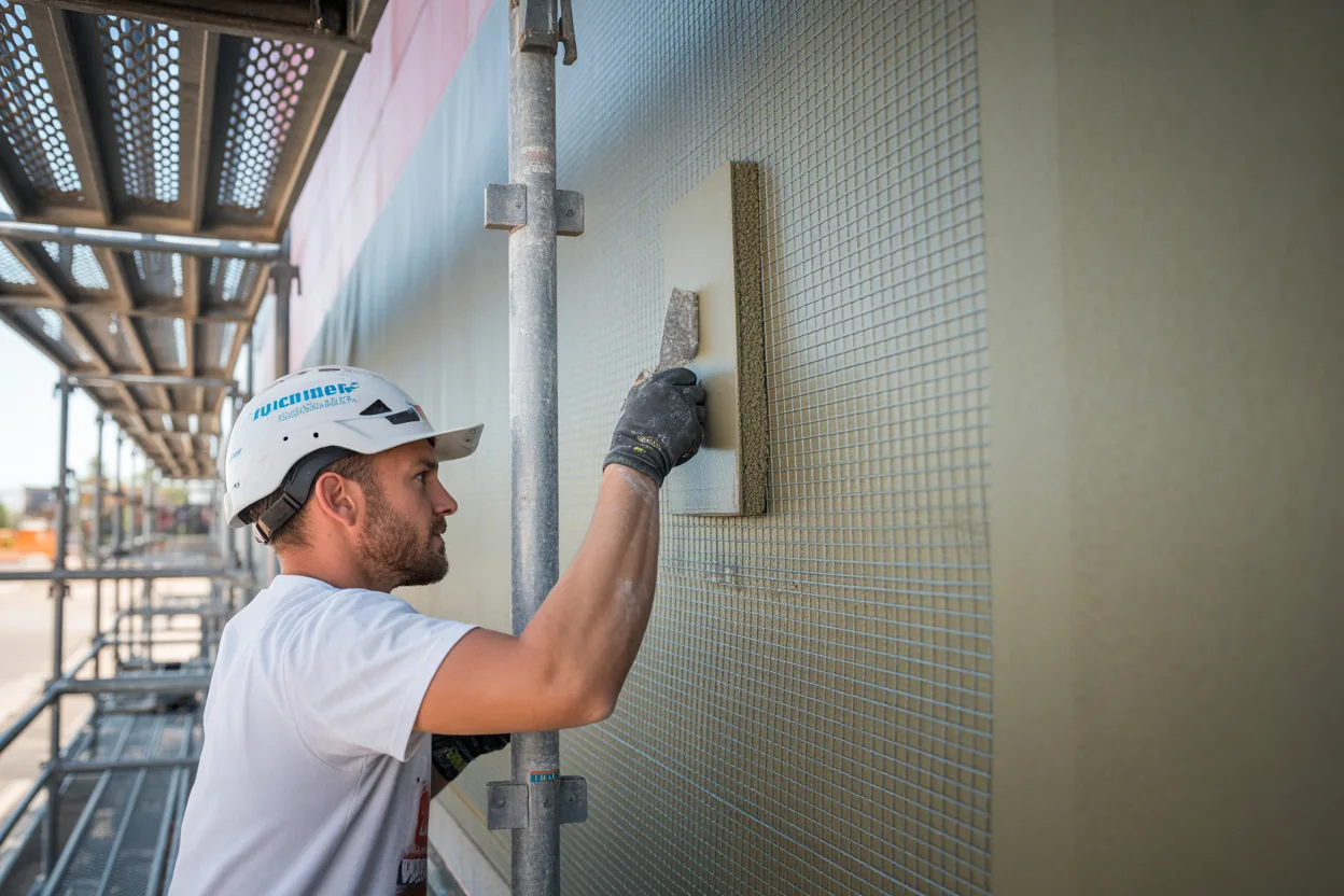 Worker applying base coat and mesh during EIFS installation on a building facade