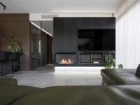 Living room at Black Wood Harmony with a linear gas fireplace set into a black media wall, an olive leather sofa and sheer curtains along the glazing