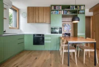 Corner view of the Cottage kitchen, with the mint-green L-shaped units, oak flooring and the fluted timber cabinet above the dining table