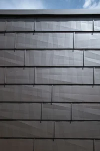 Close-up of the Cottage facade showing the faceted dark fibre-cement shingles and their exposed fixings against the sky