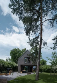 The Cottage seen from the garden beneath a tall pine, its dark gabled form set against a bright cloudy sky