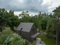 Aerial view of the Cottage from above the treetops, showing the dark shingle roof folding continuously down the gable walls