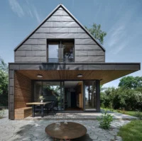 Front elevation of the Cottage, where the dark cladding lifts to reveal a warm timber-lined loggia with a built-in bench and dining table