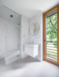 Bathroom in the Cottage lined in white terrazzo, with a walk-in shower, wall-hung basin and a timber-framed door to the balcony