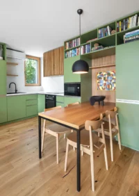 Kitchen and dining space in the Cottage, with mint-green cabinetry, a book-filled shelf run, oak table and a black dome pendant