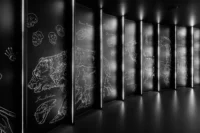 Ice age animals drawn in fine white line work across black wall panels lit by vertical LED strips at Dinosauria Museum Prague
