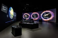 Interactive gallery at Dinosauria Museum Prague with a projected Earth, three dinosaurs framed in glowing rings on the media wall and touch consoles