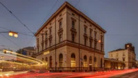 The Masarykovo nádraží station building at dusk with tram light trails sweeping across the foreground