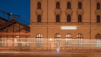 Night view of the Masaryčka facade beside the station's glazed platform hall, with long light trails from passing trams