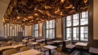Corner of Masaryčka Restaurant with small tables along the tall arched windows, lit by the timber ceiling installation