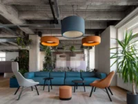 Seating area with a blue modular sofa, orange and blue drum pendants and a yucca palm beside the window at Office That Breathes in Prague