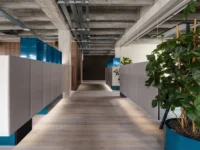 Corridor lined with grey upholstered storage walls topped in blue metal, lit from below along the oak floor at Office That Breathes