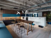 Dining area at Office That Breathes with a walnut high table, black stools, teal upper cabinets and slim tubular pendant lights
