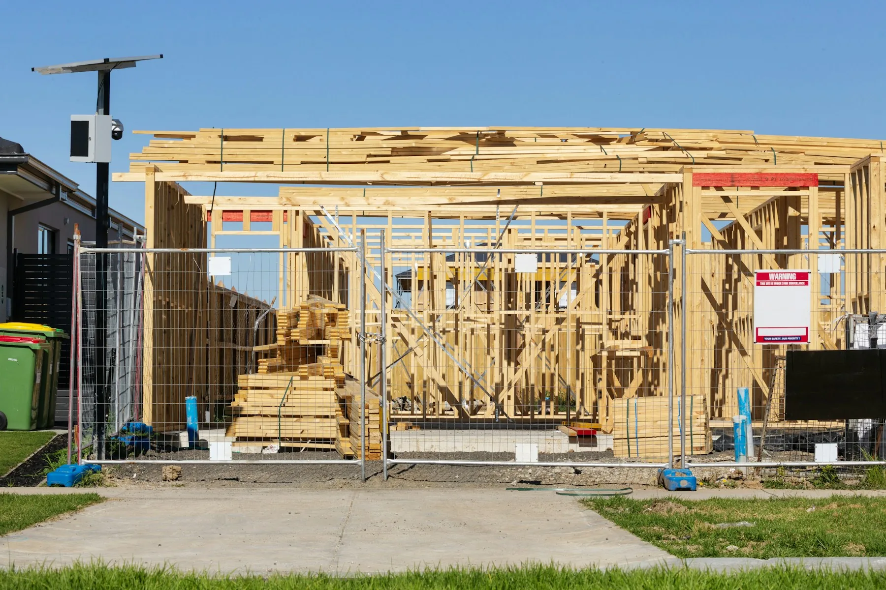 Timber frame of a new house under construction behind a site fence
