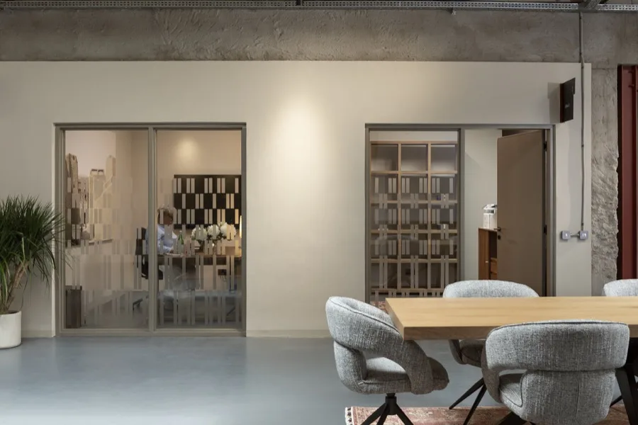 Interior with glazed partitions, patterned screens and a light timber table under a concrete beam