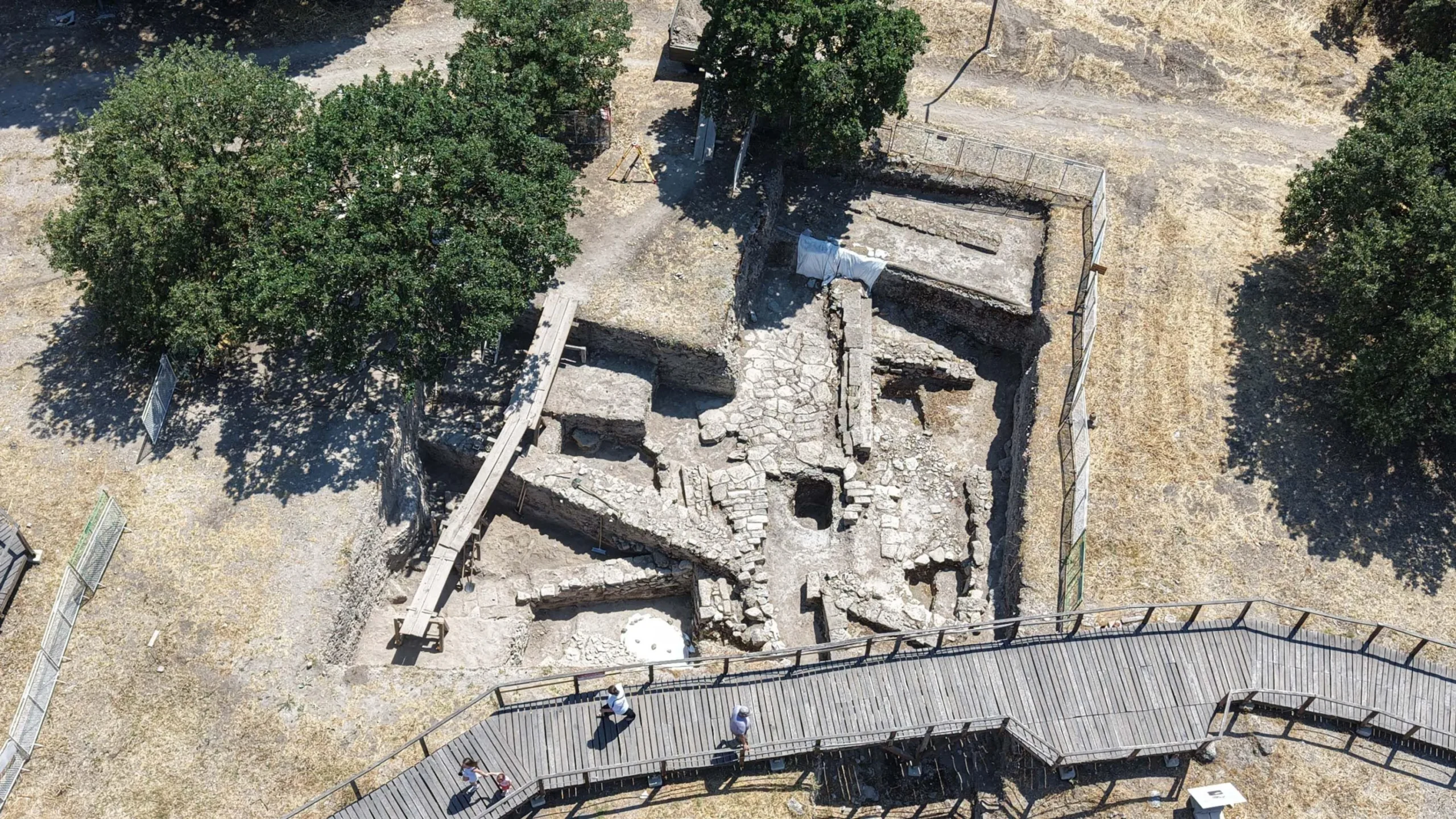 Aerial view of stone wall foundations and rubble at an excavation site bordered by a wooden walkway