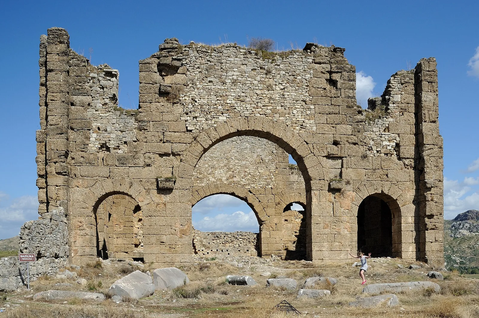 Ruined stone basilica with tall arched openings on the acropolis of Aspendos