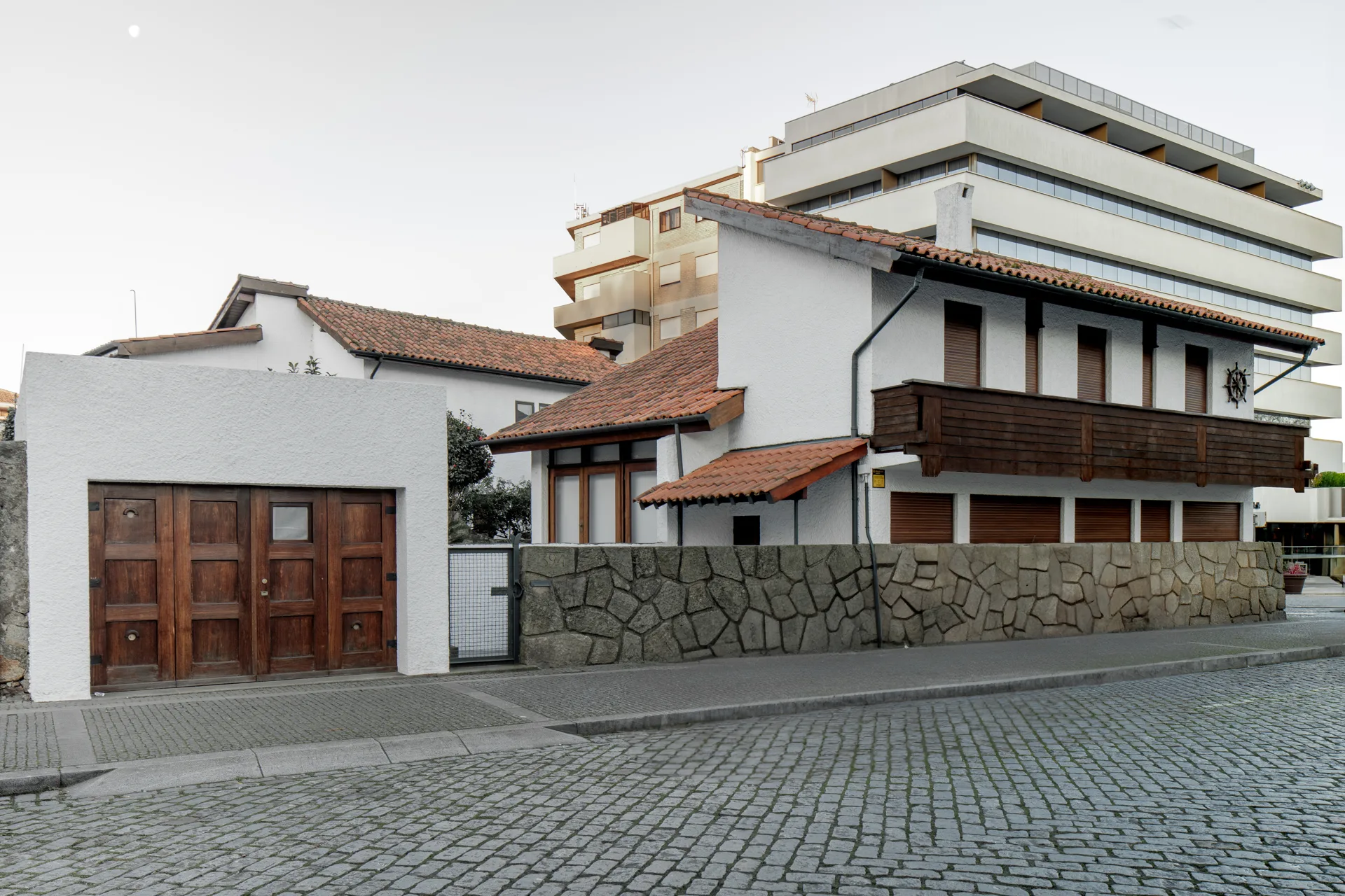 White rendered street facade with its tiled roof and stone boundary wall, Casa d’Abreu Neto by Álvaro Siza