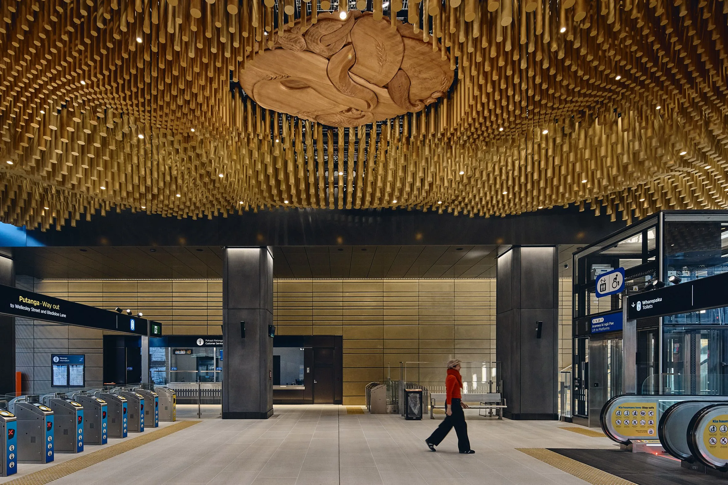 Underground station hall with a ceiling of thousands of hanging wooden rods forming a swirling pattern above turnstiles