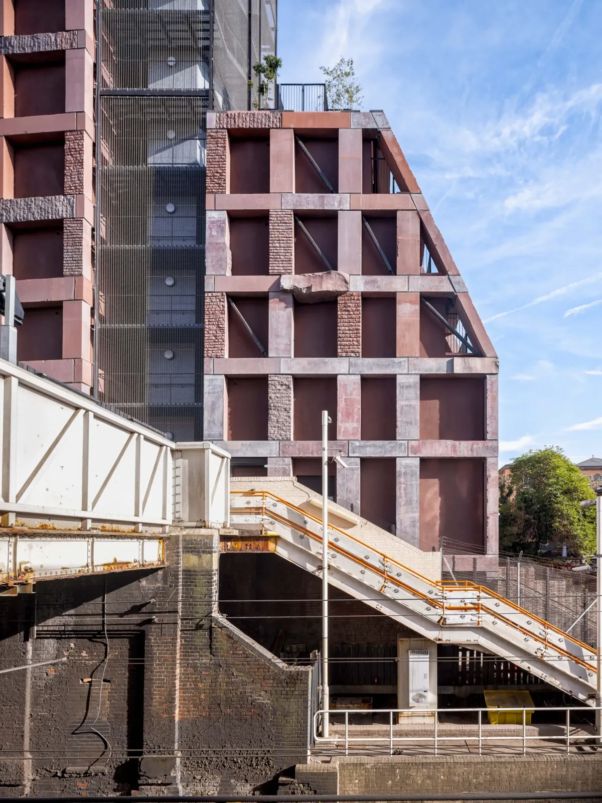 Rough and smooth granite frame of the building rising above a railway bridge and metal stairs