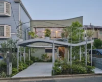 House in Nakano seen from the street at dusk with the curved planted terrace lit above the entrance