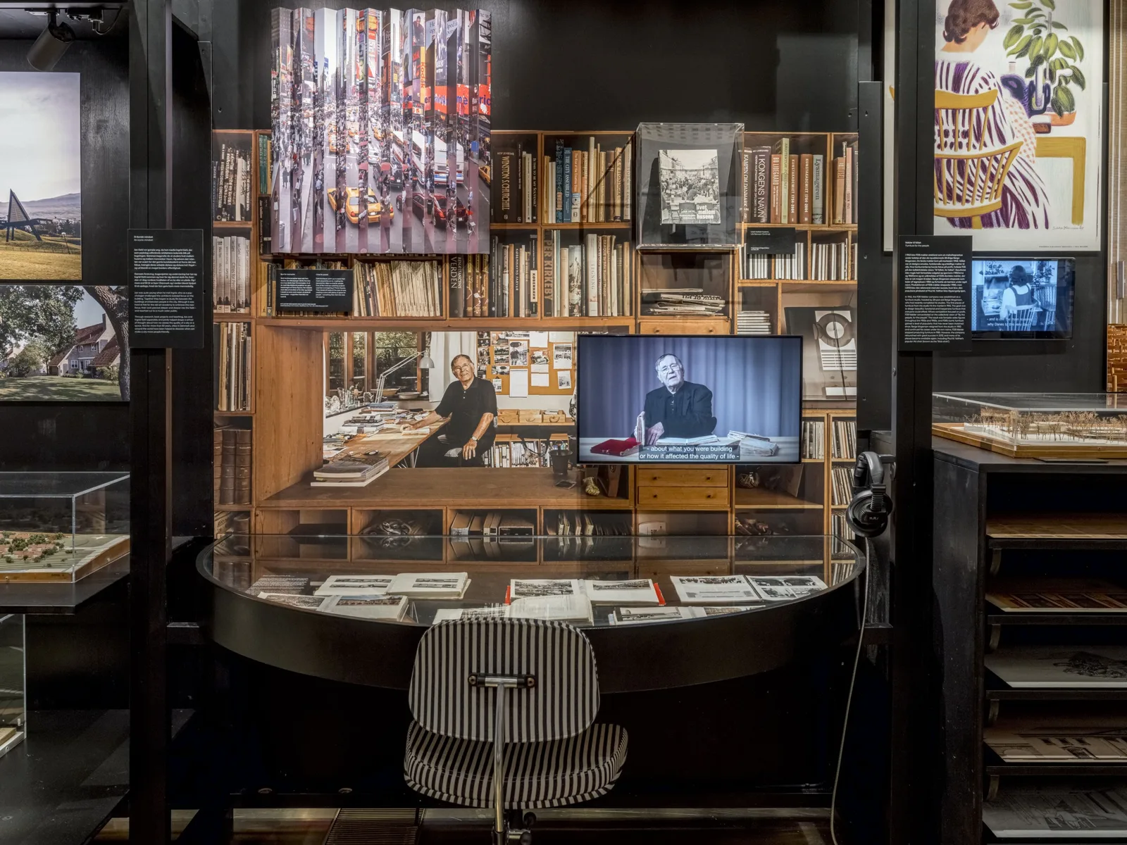 Exhibition space with a recreated wooden study, bookshelves, a desk and a screen showing an interview