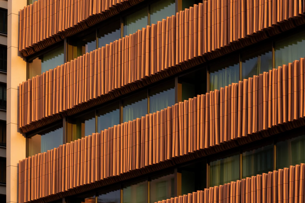 Terracotta baguette louvres on a glazed office facade lit by low evening sun