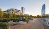 Waterfront boardwalk with benches and planted beds beside the curved residential buildings and glass towers