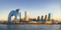 The low-rise buildings along the shore seen from the water, with a crescent-shaped tower and high-rises behind