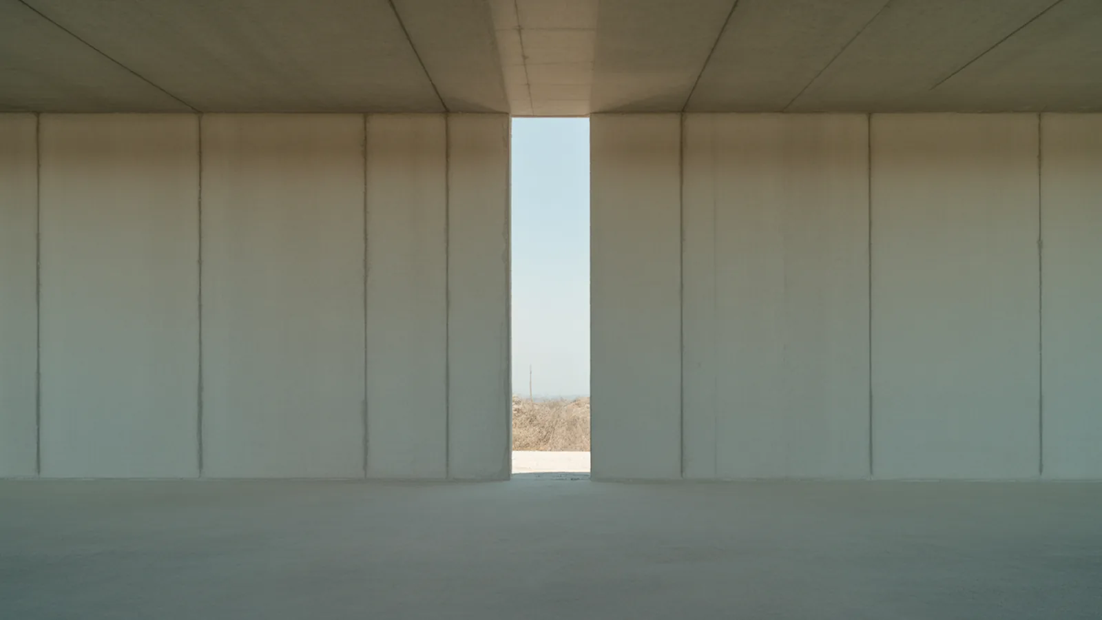 Bare smooth concrete wall with a narrow full-height slot of daylight grazing the surface