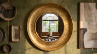 Olive plaster wall with a hammered brass round mirror, ceramic plates and framed art