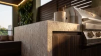 Outdoor kitchen counter in rough stone with a steel grill beside dark timber panels