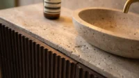 Travertine vessel sink on a fluted dark timber vanity with a brass tap