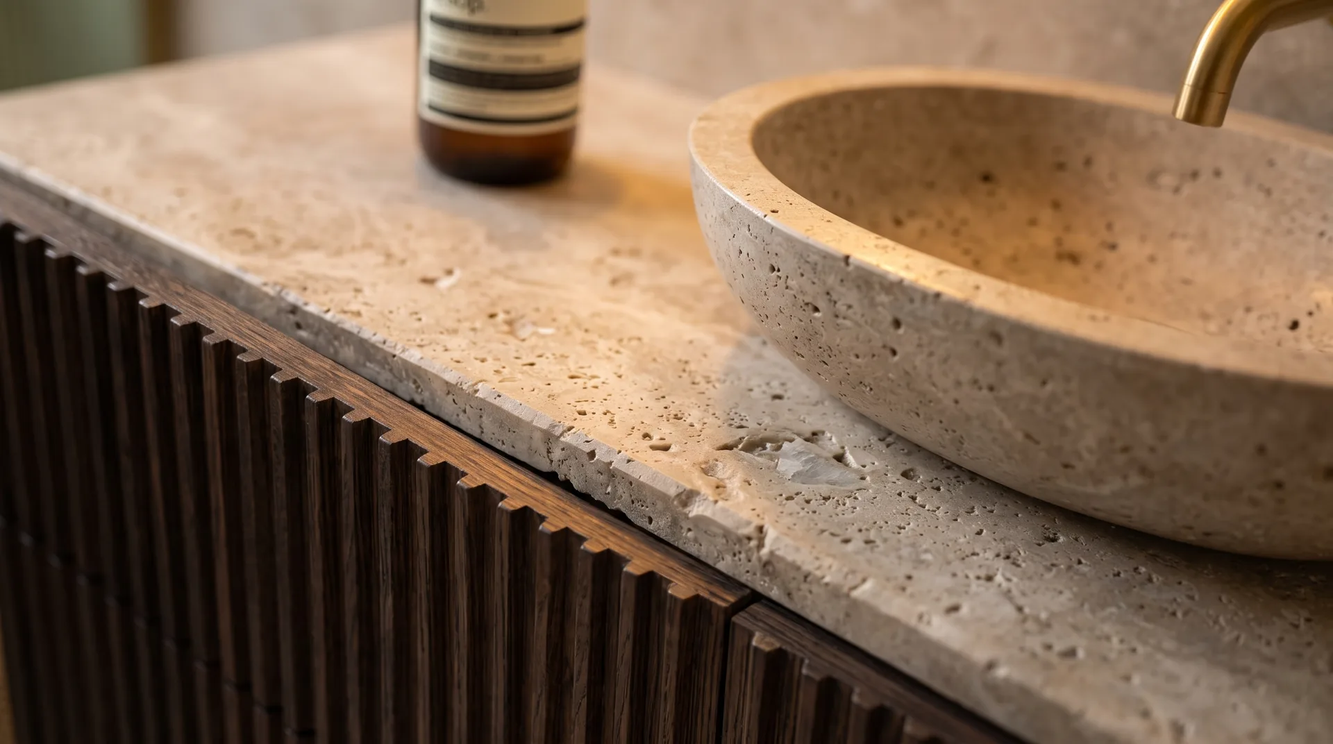 Travertine vessel sink on a fluted dark timber vanity with a brass tap