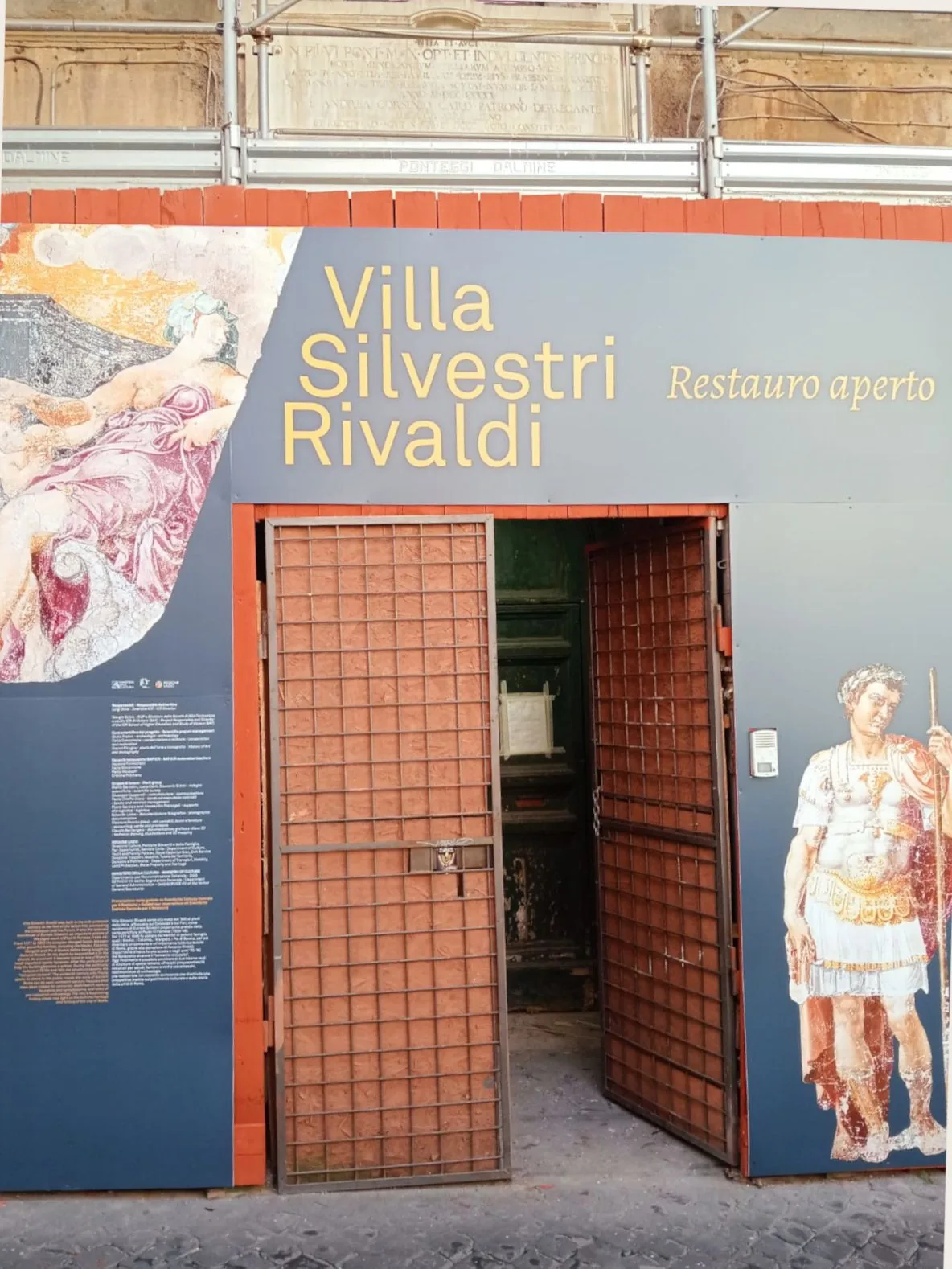 Entrance gate with a banner reading Villa Silvestri Rivaldi and painted classical figures beside open metal doors