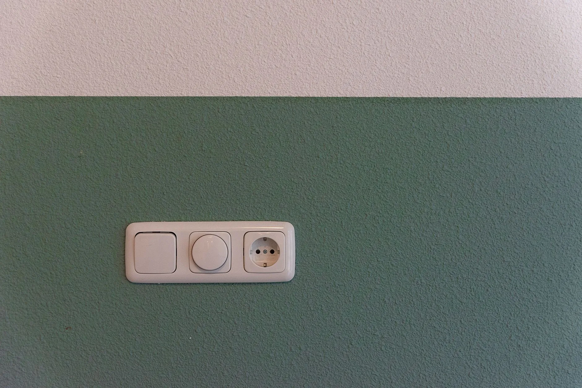 White switch, rotary dimmer and socket mounted together on a green painted wall
