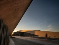 View from under a timber soffit toward the curved library volume across a brick paved forecourt