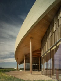 Sweeping curved roof edge with timber soffit, slender columns and a glazed facade at the entrance