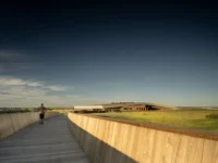 Visitor walking along a timber walled ramp that curves toward the library across the prairie