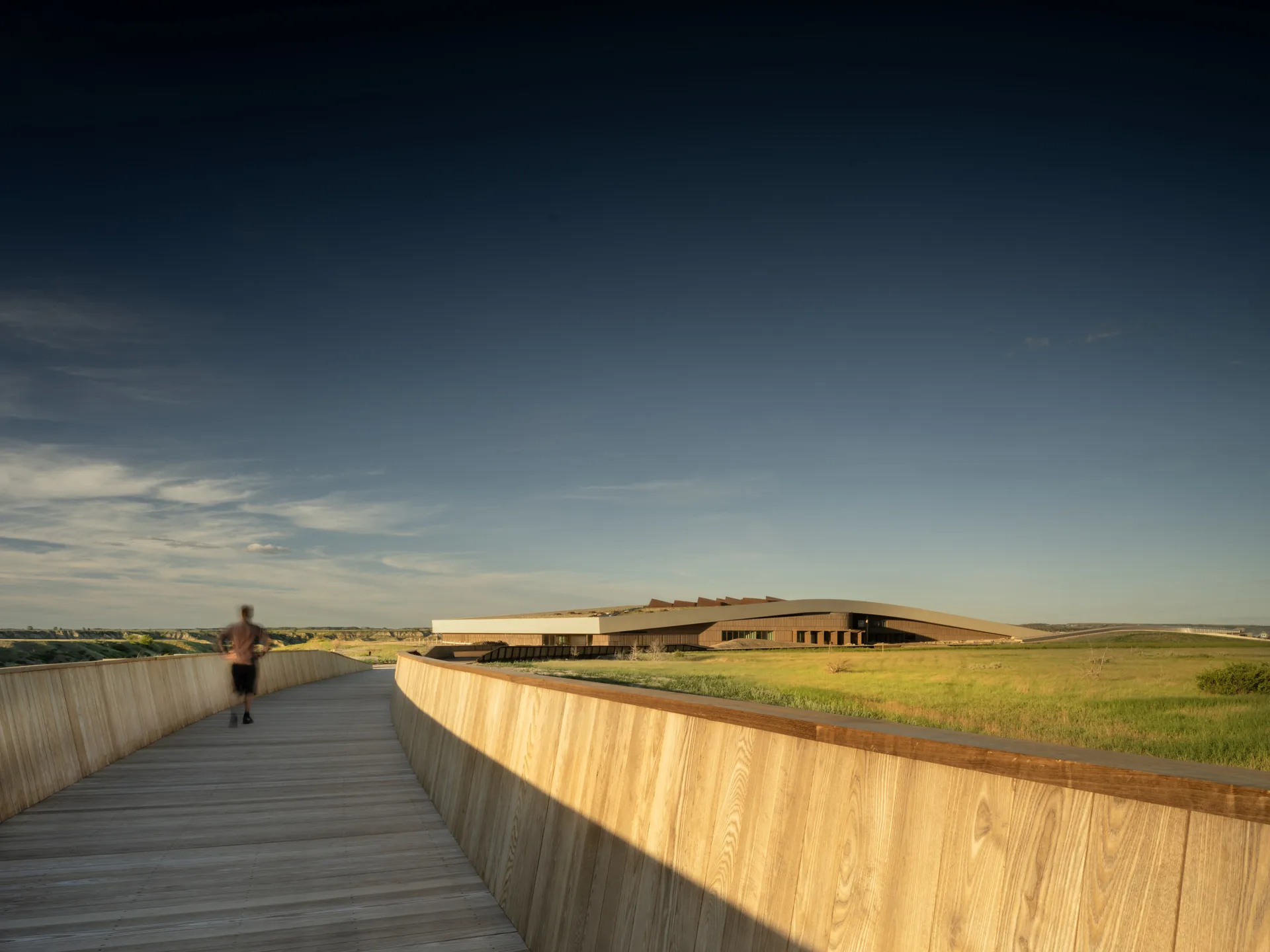 Visitor walking along a timber walled ramp that curves toward the library across the prairie