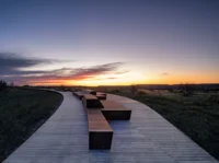 Elevated boardwalk with long steel benches curving across the prairie at sunset